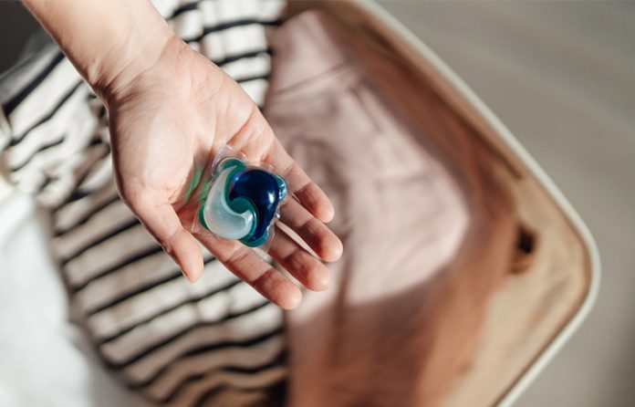 Laundry detergent pod in hand over wash basket